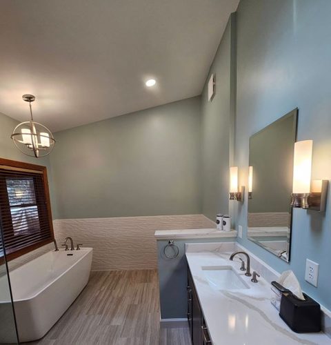 Bathroom with a freestanding tub, white quartz vanity top, wall sconces and textured wainscot tile