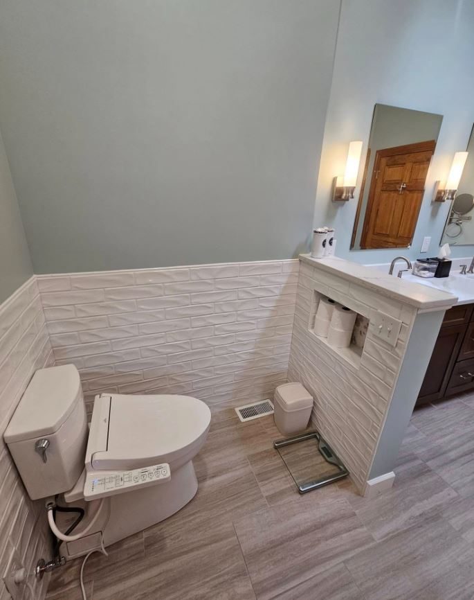 Bathroom with textured white wainscot tile, a tiled half wall with niche, and a bidet-seat toilet