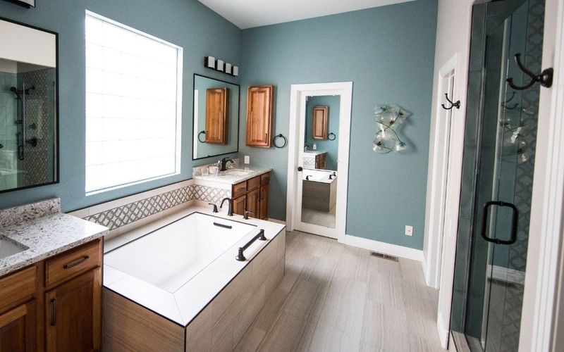 Drop-in soaking tub beside wood vanities and teal walls