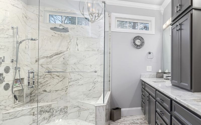 Marble-look bathroom with frameless shower and grey cabinetry