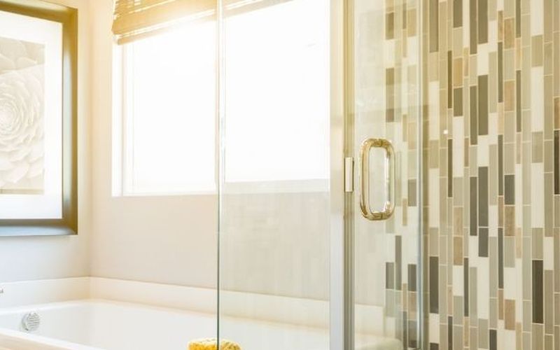 Glass shower door beside a bathtub and mosaic tile